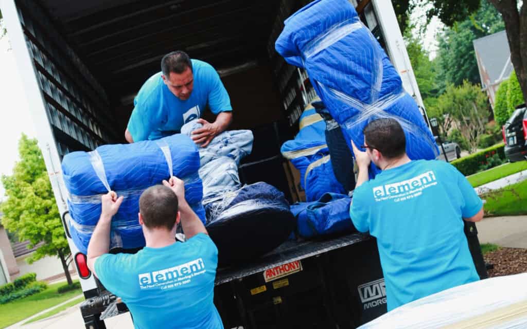 Movers in Element shirts loading blanket-wrapped furniture into the back of a truck